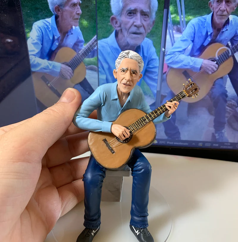 Miniatura esculpida de senhor idoso tocando violão com a foto original ao fundo